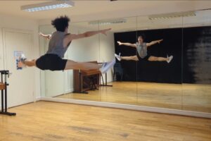 ダンススタジオで開脚ジャンプをする天羽