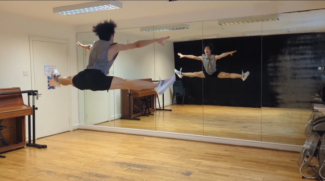 ダンススタジオで開脚ジャンプをする天羽
